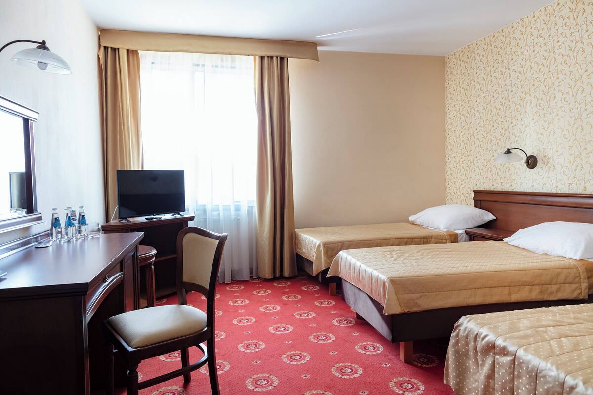 A hotel room with a desk, chair, television, two beds, and a carpeted floor.
