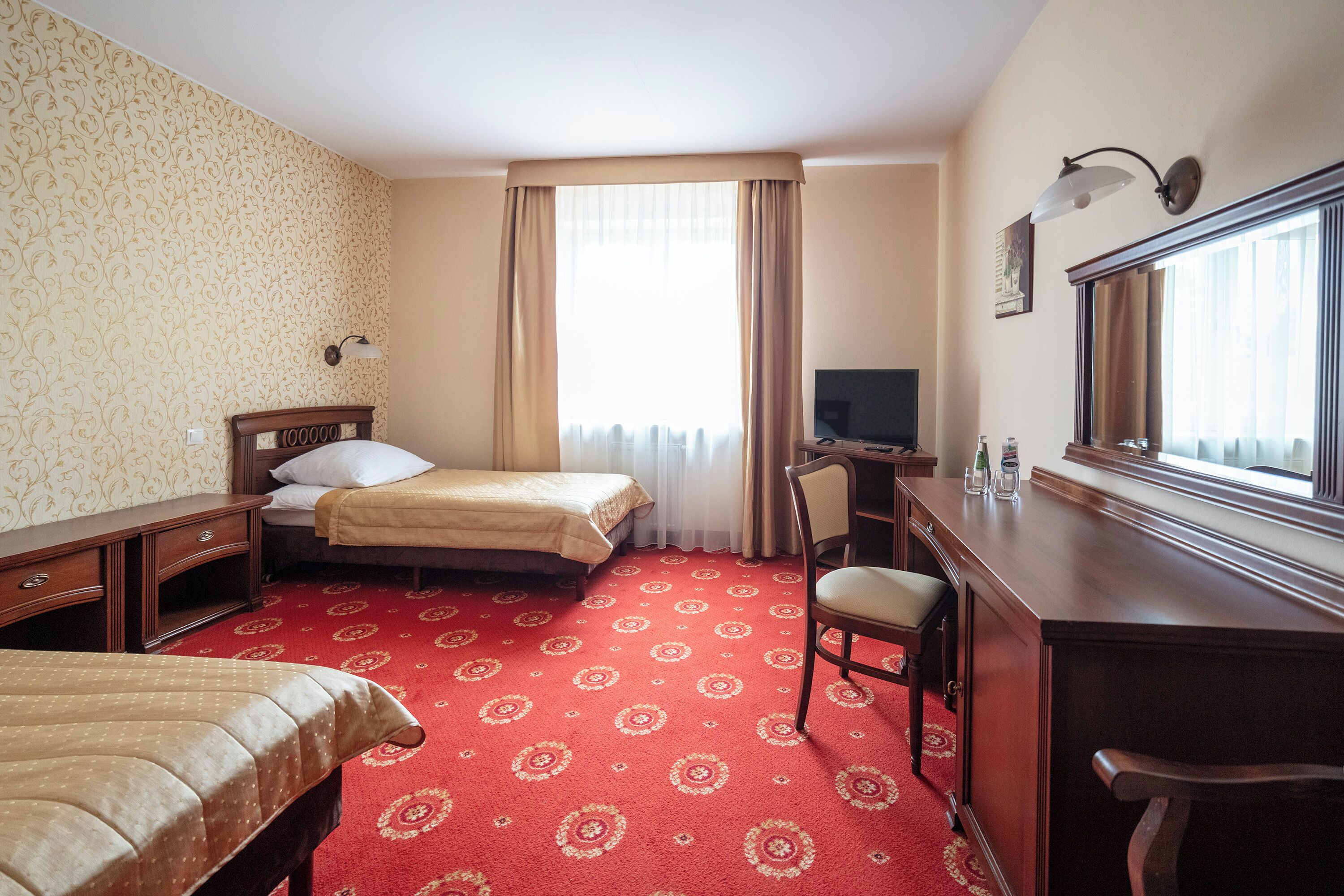 Habitación de hotel con dos camas, un escritorio, una silla, un televisor y una ventana con cortinas.