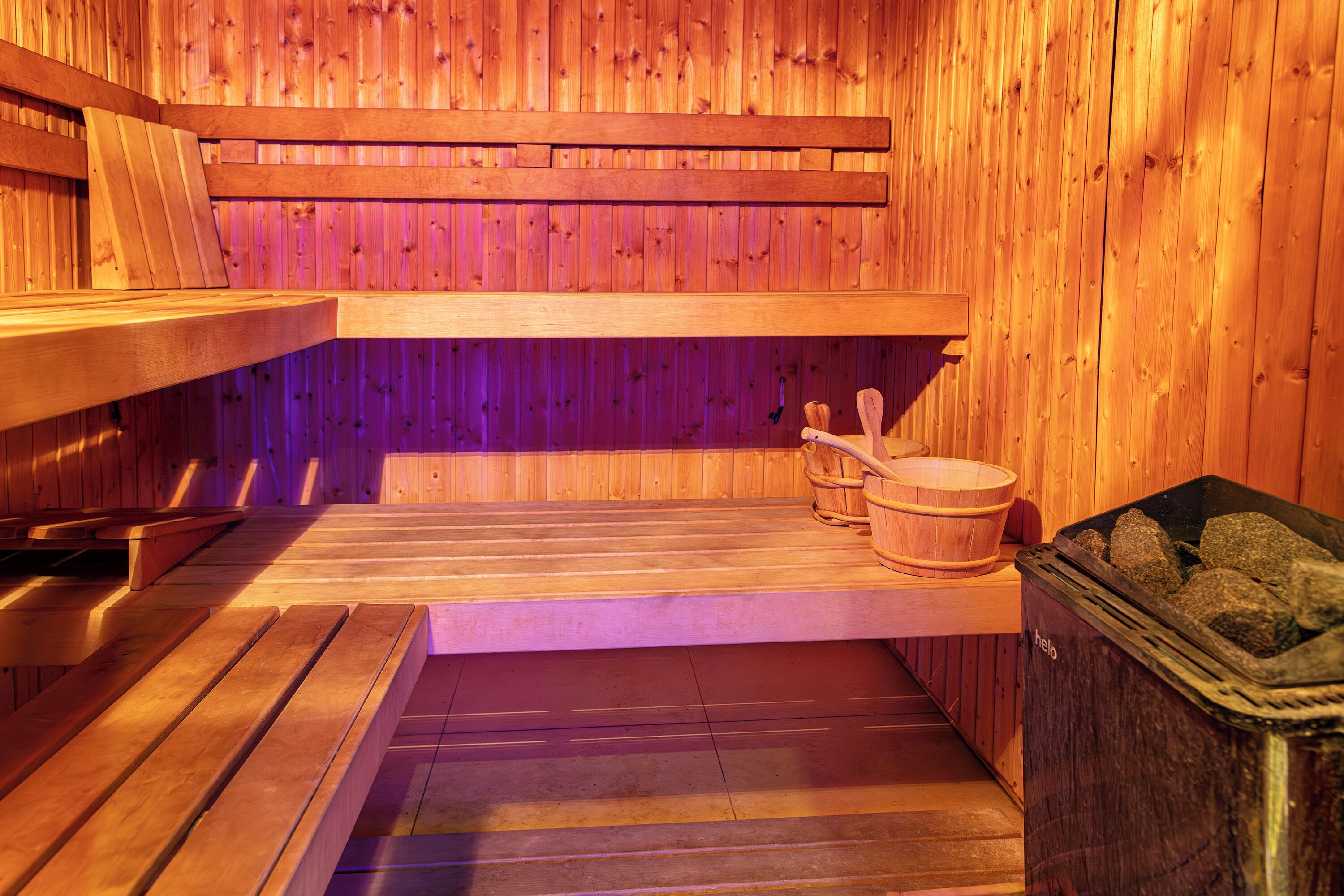 Uma sauna com bancos de madeira, uma mesa de madeira, um balde de madeira e uma lixeira.