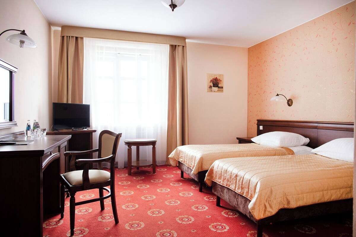A hotel room with two beds, a desk with a chair, a television, and a window with curtains.