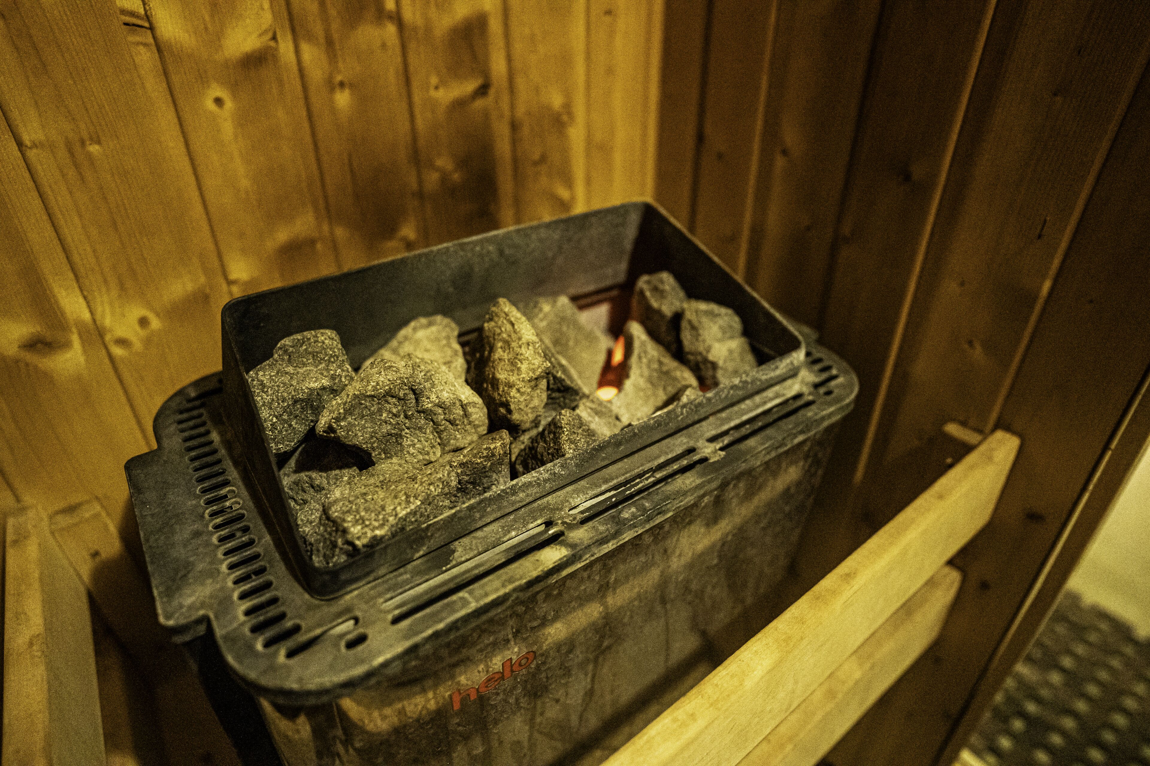 Un contenedor metálico con rocas y fuego encendido, apoyado contra una pared de madera.