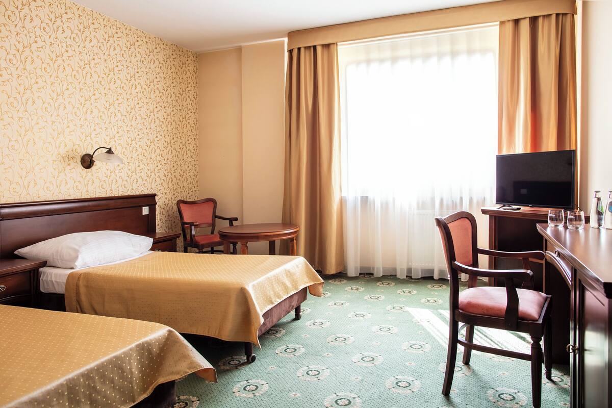 A hotel room with two beds, a desk, a chair, a television, and a window with curtains.