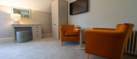 A modern room with a desk, two chairs, a radiator, and a TV on the wall.