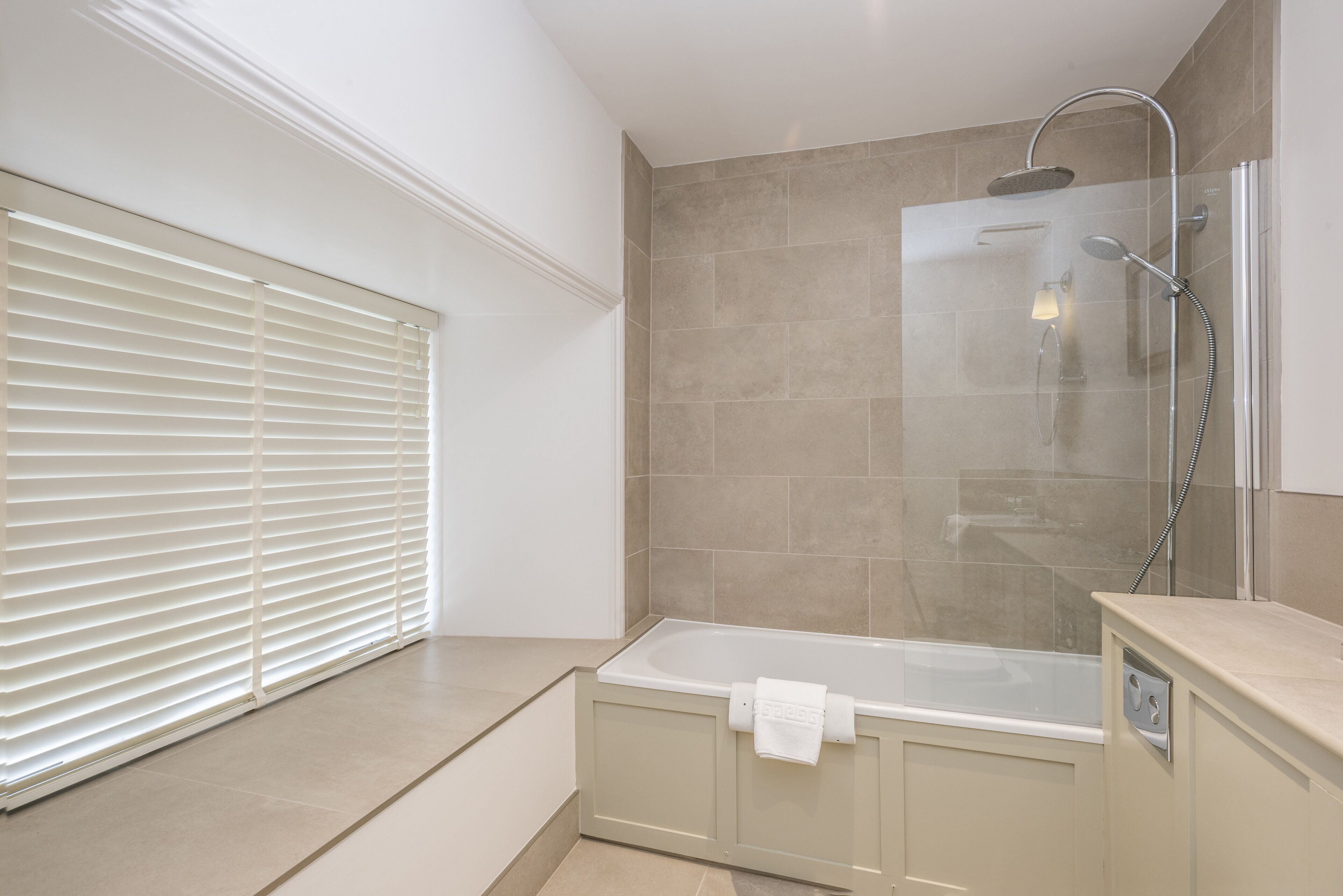 A modern bathroom with a glass-enclosed shower, a bathtub, and a window with blinds.