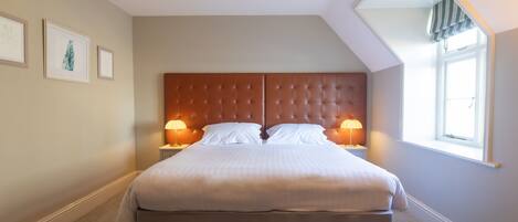 A neatly made bed with a tufted headboard, two bedside lamps, and a large window with a view of the sky.