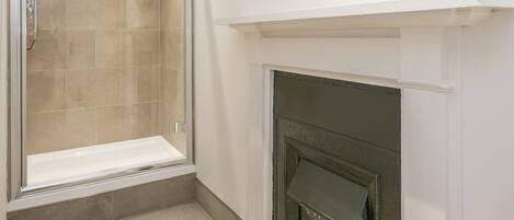 A bathroom with a glass-enclosed shower, a white tiled floor, and a fireplace with a white mantel.