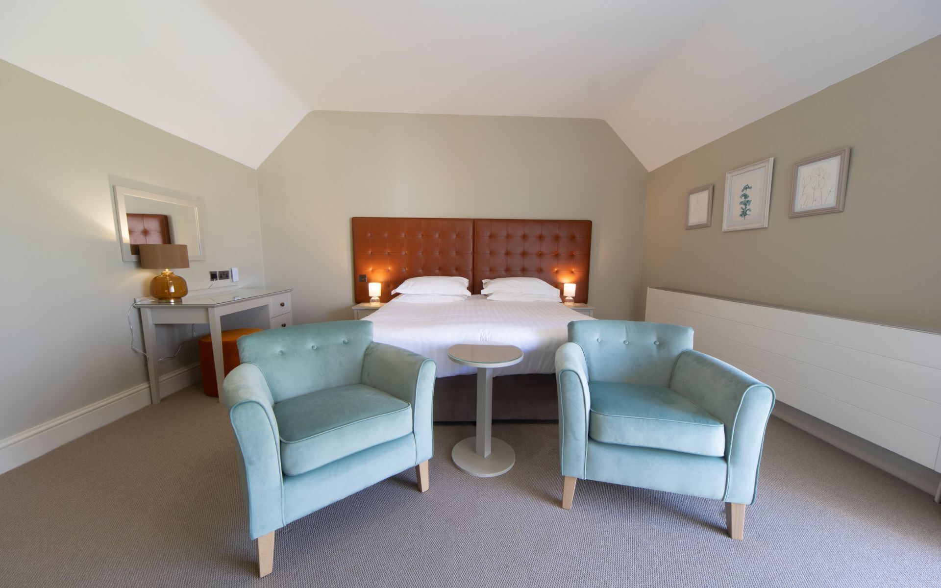 A hotel room with a large bed, two armchairs, a small table, a desk, and a mirror.