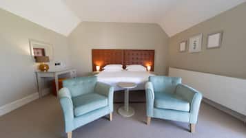 A hotel room with a large bed, two armchairs, a small table, a desk, and a mirror.