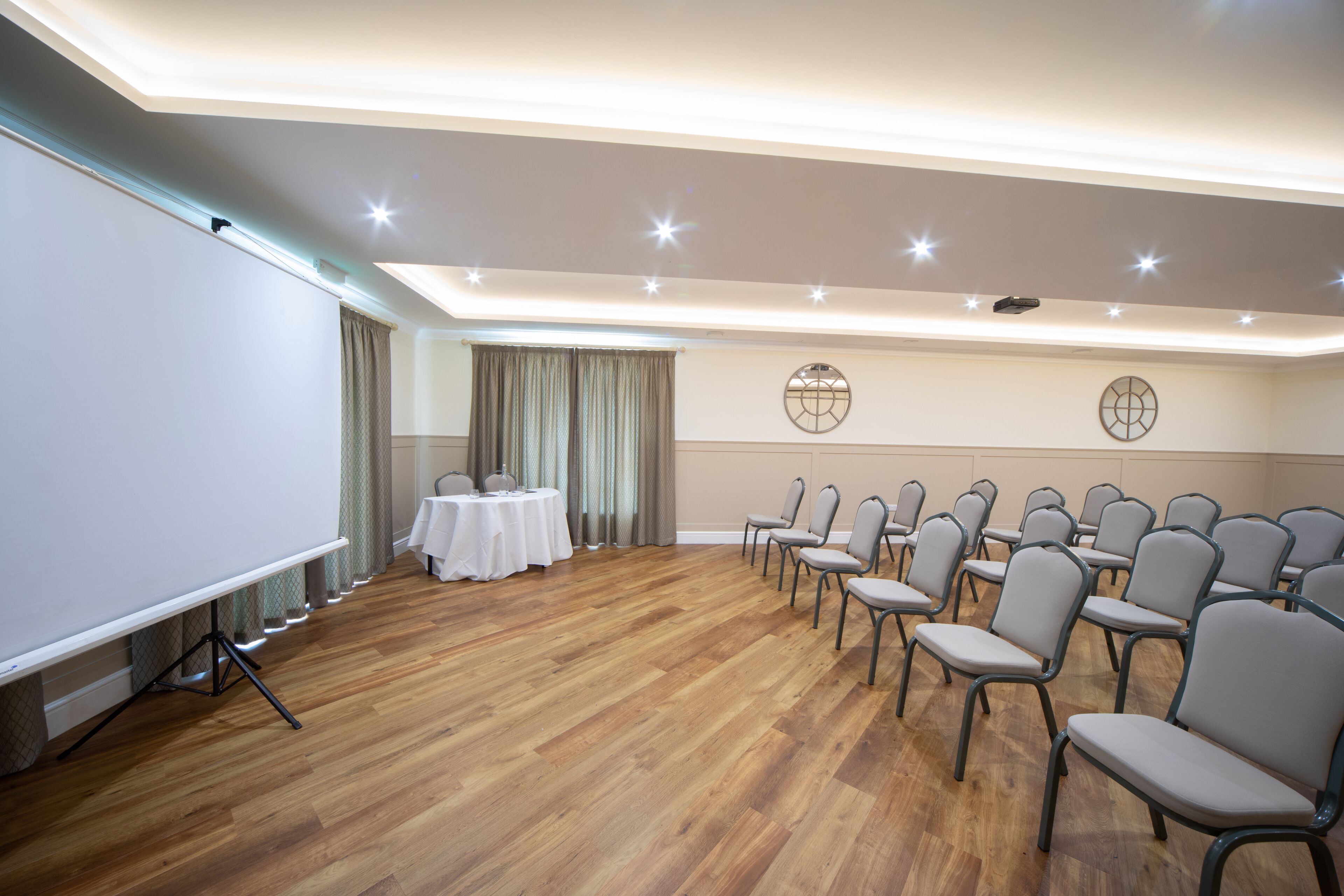 A conference room with a projector screen, a table with chairs, and rows of chairs facing the screen.