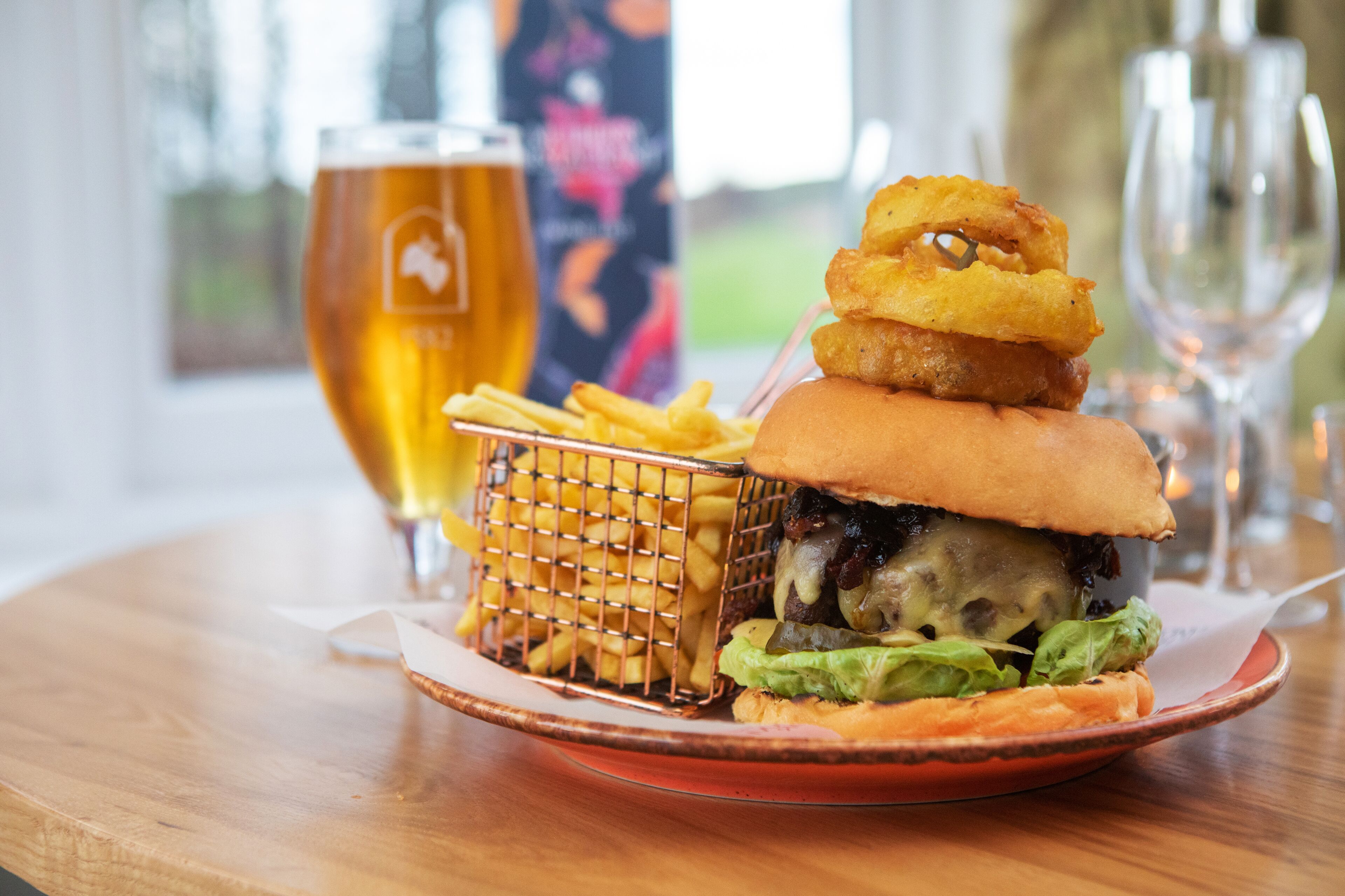 Una hamburguesa con papas fritas y un vaso de cerveza sobre una mesa de madera.