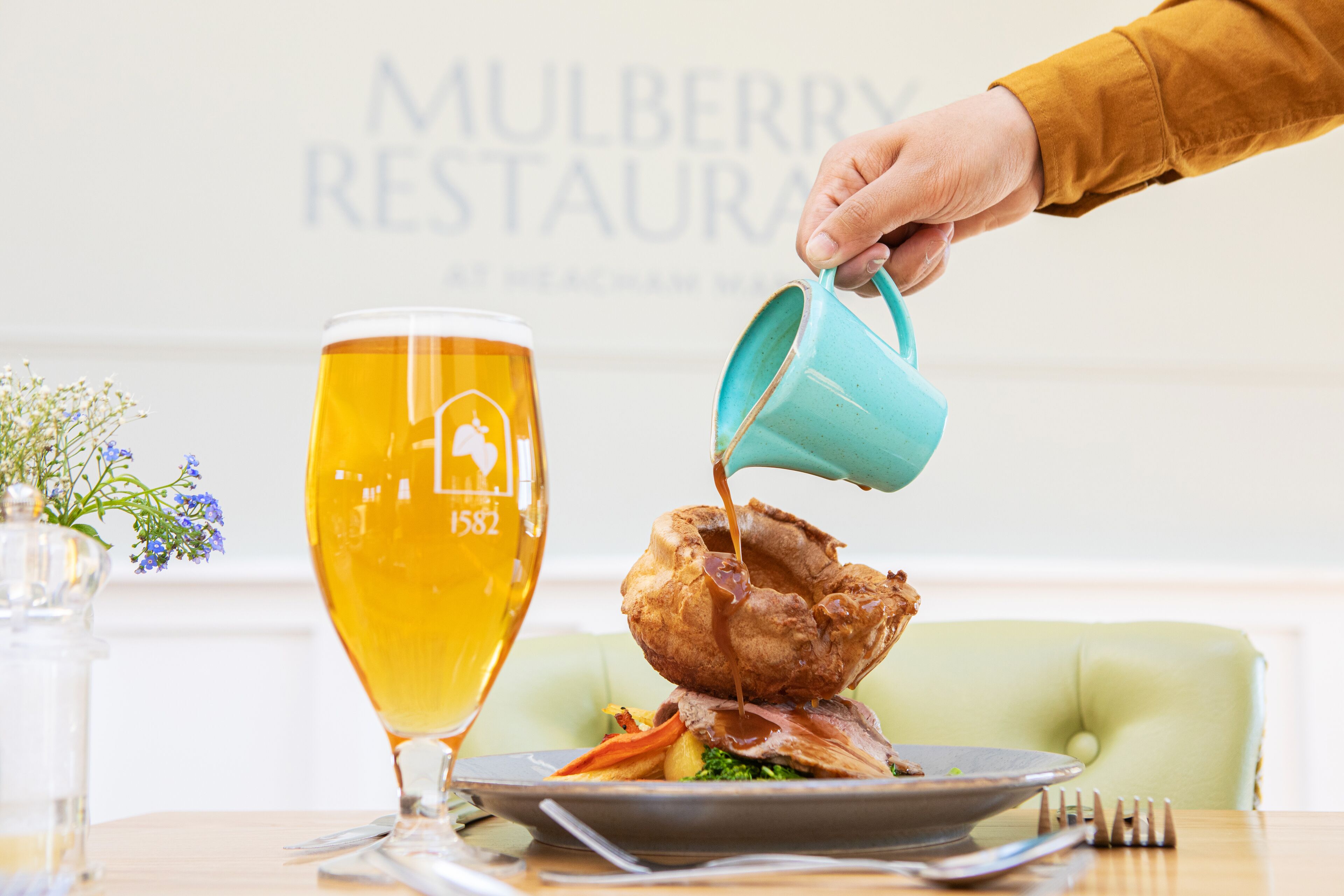 A person pouring a drink into a glass next to a plate with food.