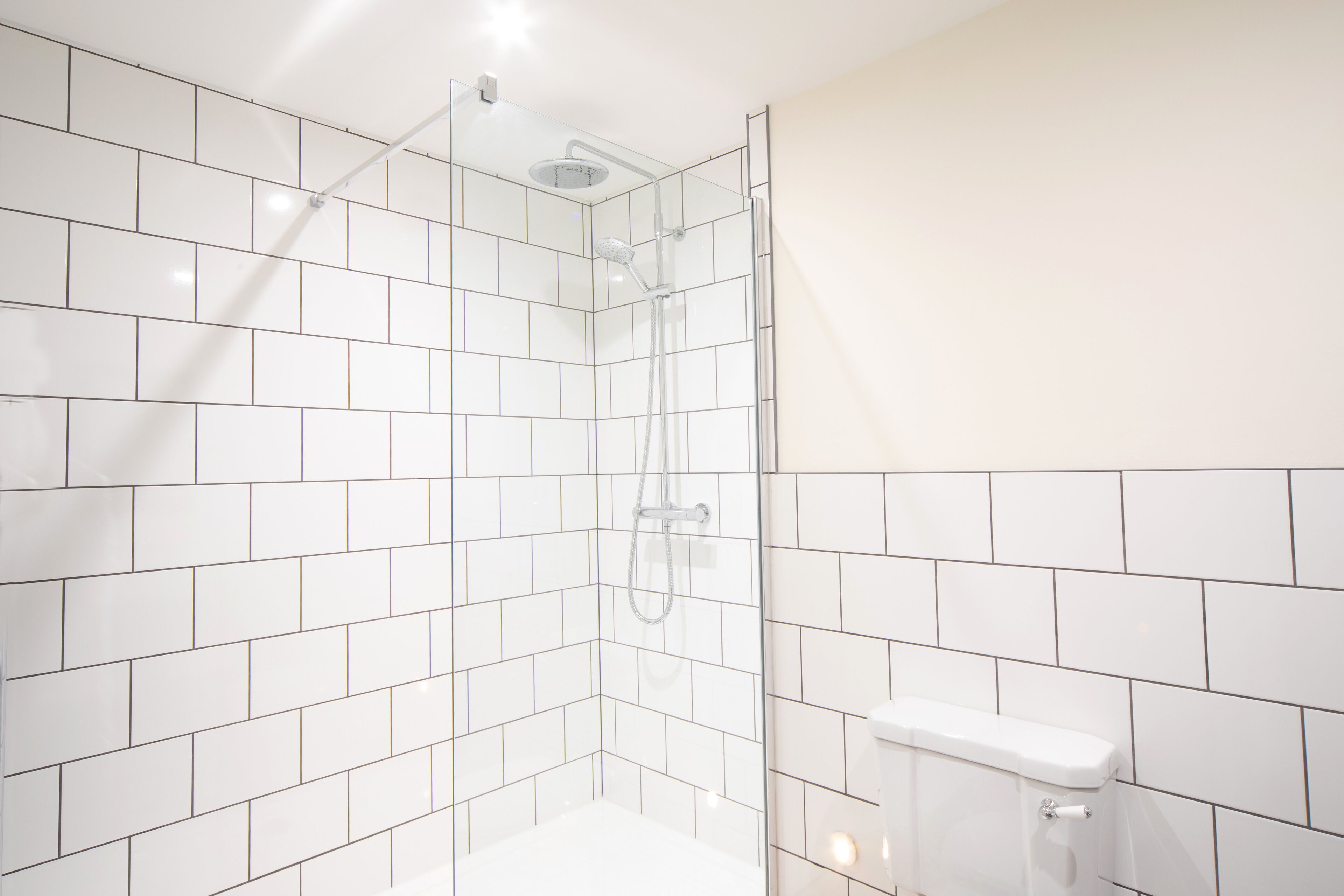 A modern bathroom with white tiles, a glass shower enclosure, and a white toilet.