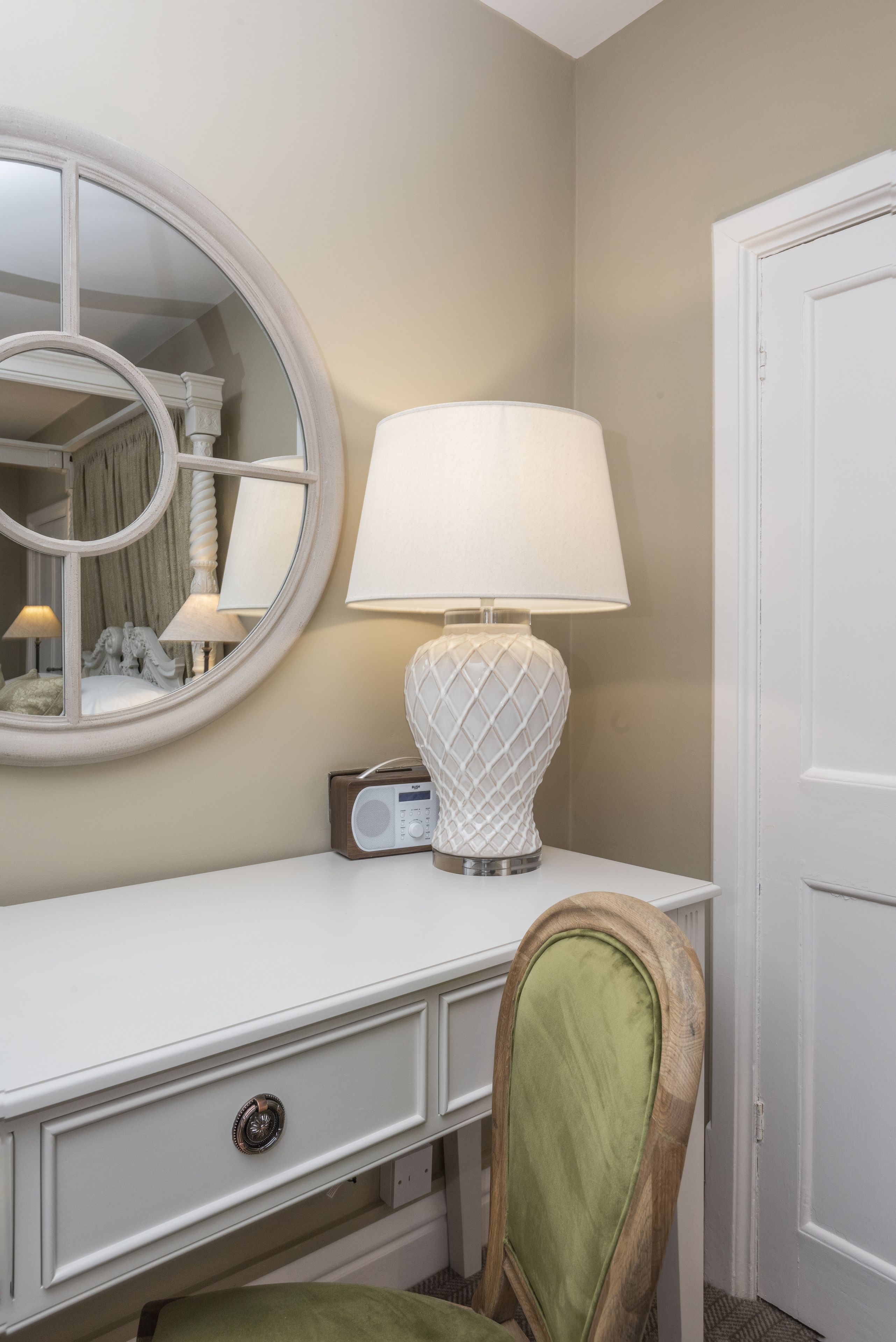 A white desk with a round mirror, a radio, and a lamp.