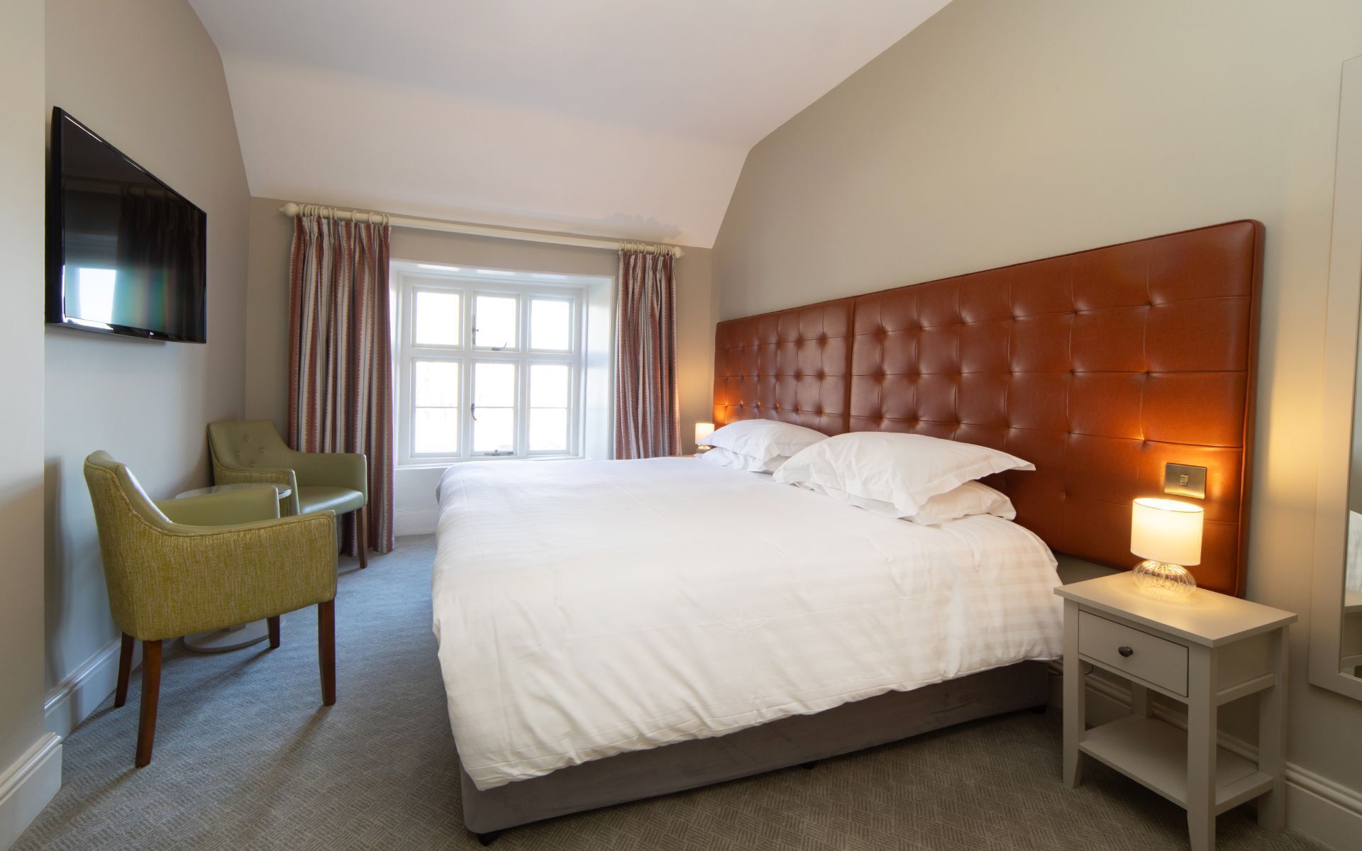 Una habitación de hotel con una cama grande, una silla, un televisor y un ventanal con cortinas.