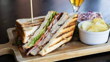 A sandwich on a wooden board with a side of chips and a glass of beer.