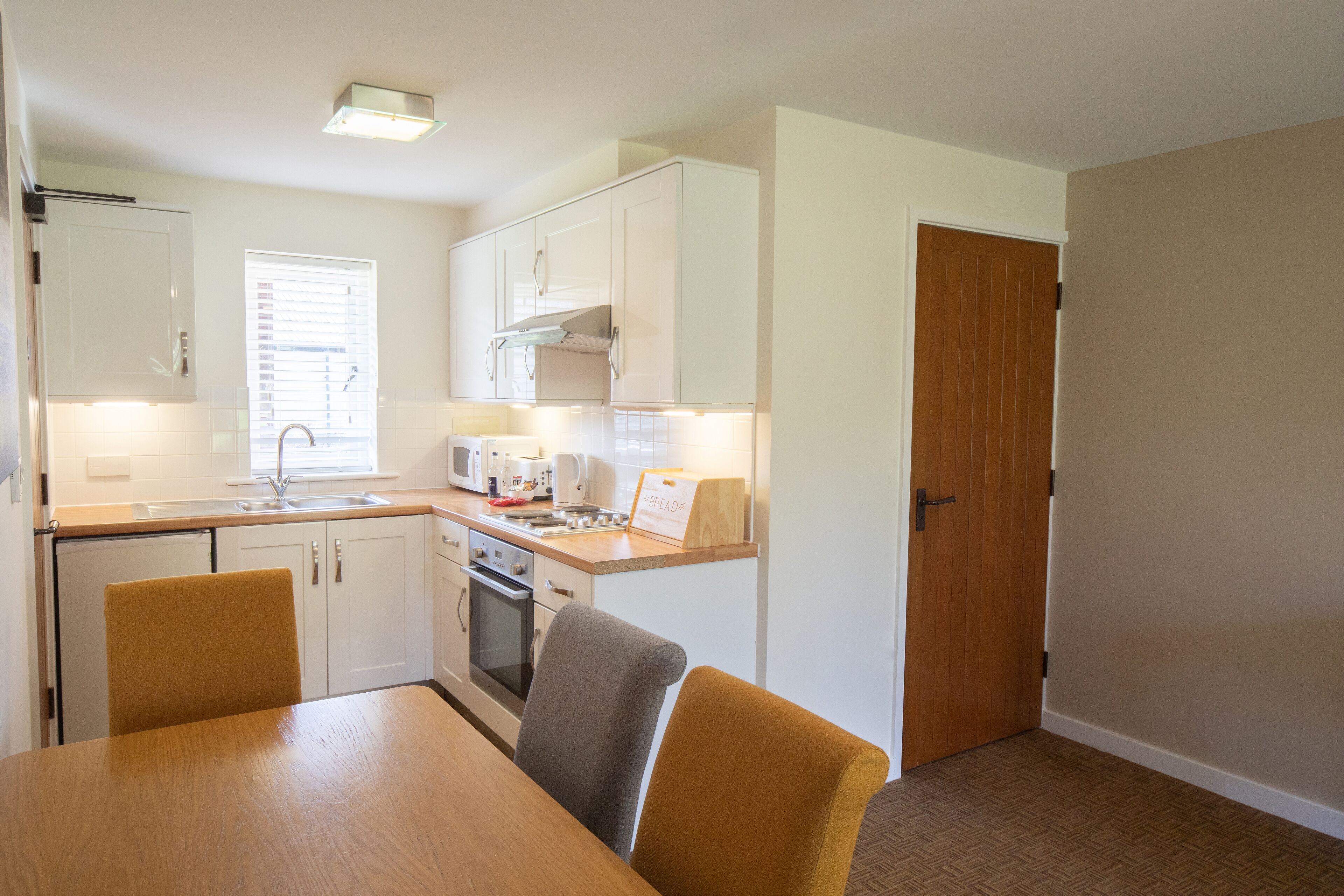 A compact kitchen with white cabinets, a microwave, a sink, and a dining area with a table and chairs.