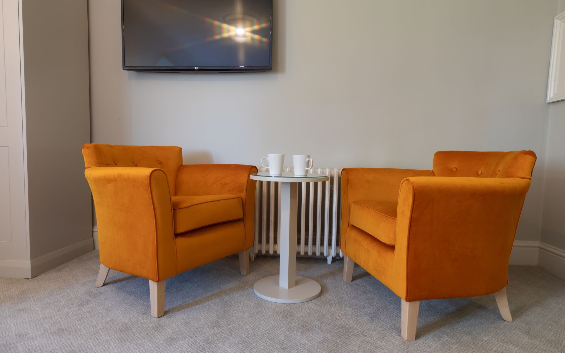 A room with two orange armchairs, a small round table with two white cups, and a white radiator.