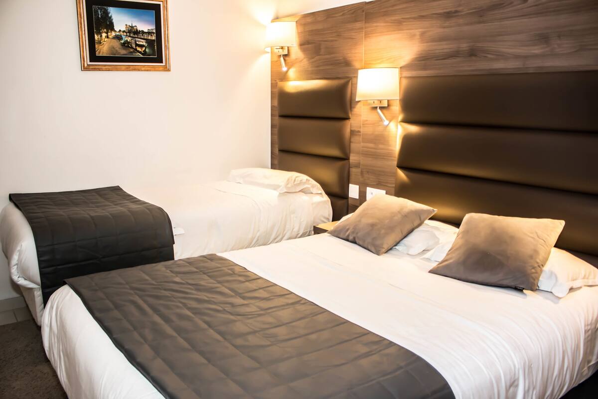 A hotel room with two beds, each with a headboard and bedside lamps.