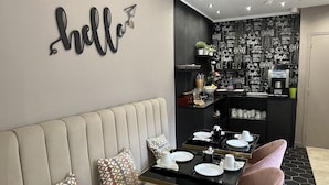 A modern cafe with a black and white chalkboard wall, a 'hello' sign, a coffee machine, and a seating area with a sofa and pink chairs. - Hotel Agenor (Paris)