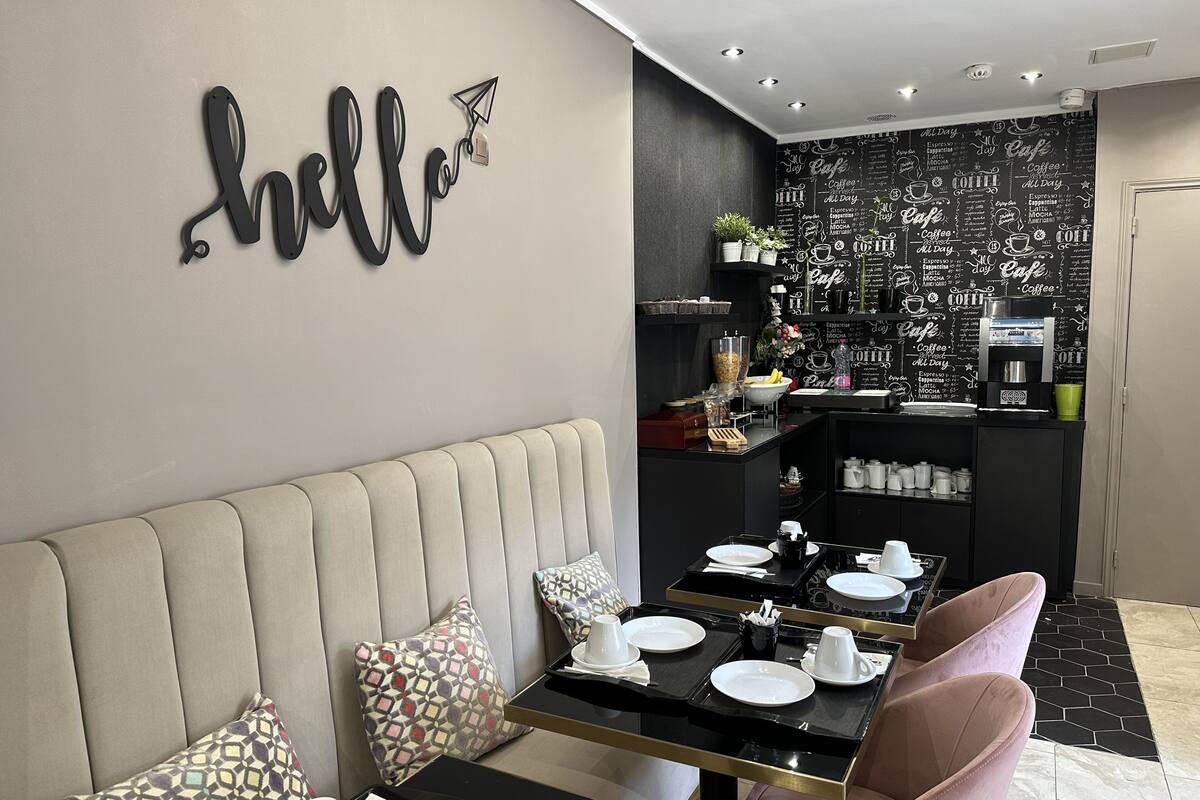 A modern cafe with a black and white chalkboard wall, a 'hello' sign, a coffee machine, and a seating area with a sofa and pink chairs.