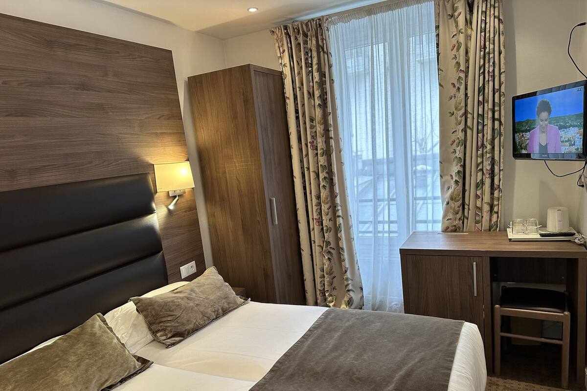 A hotel room with a bed, a desk, a TV, and curtains.