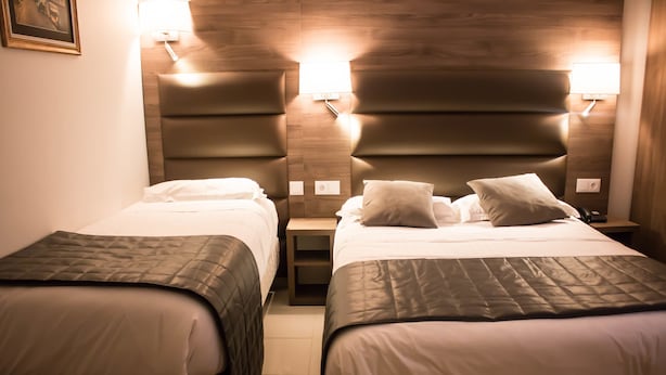 A hotel room with two beds, each with a headboard and bedside lamps. - Hotel Agenor (Paris)