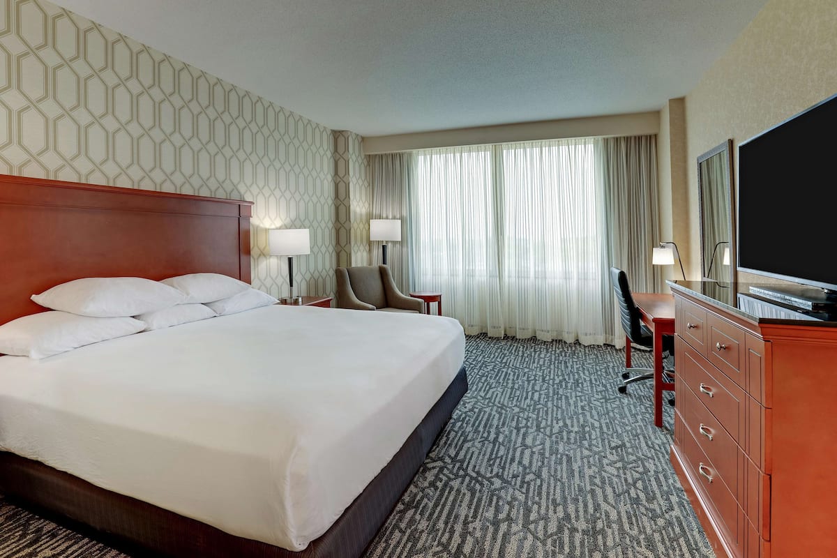 Une chambre d’hôtel avec un grand lit, un bureau avec une chaise, une télévision et une commode.