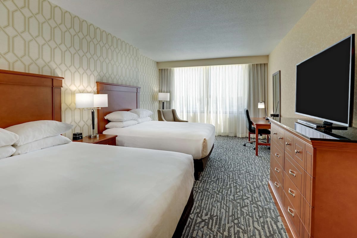 Une chambre d’hôtel avec deux lits, une commode, un téléviseur et un bureau avec une chaise.