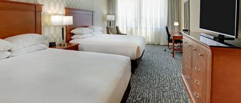 A hotel room with two beds, a dresser, a television, and a desk with a chair.