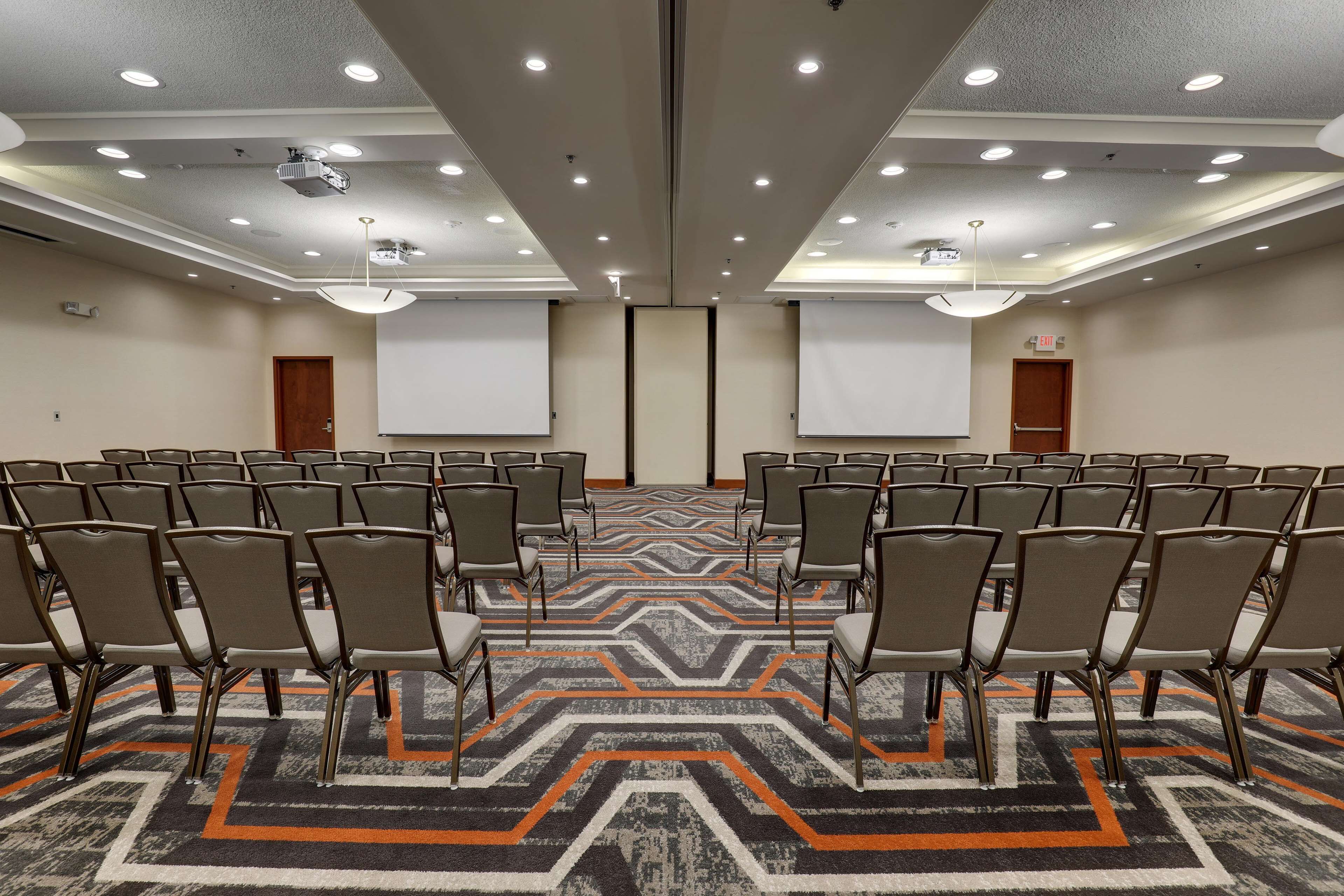 A conference room with rows of chairs, a carpeted floor, and a projector screen.