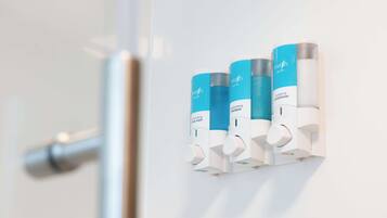 Ein Badezimmer mit einem an der Wand befestigten Spender, der drei Flaschen Haarpflegeprodukte enthält.
