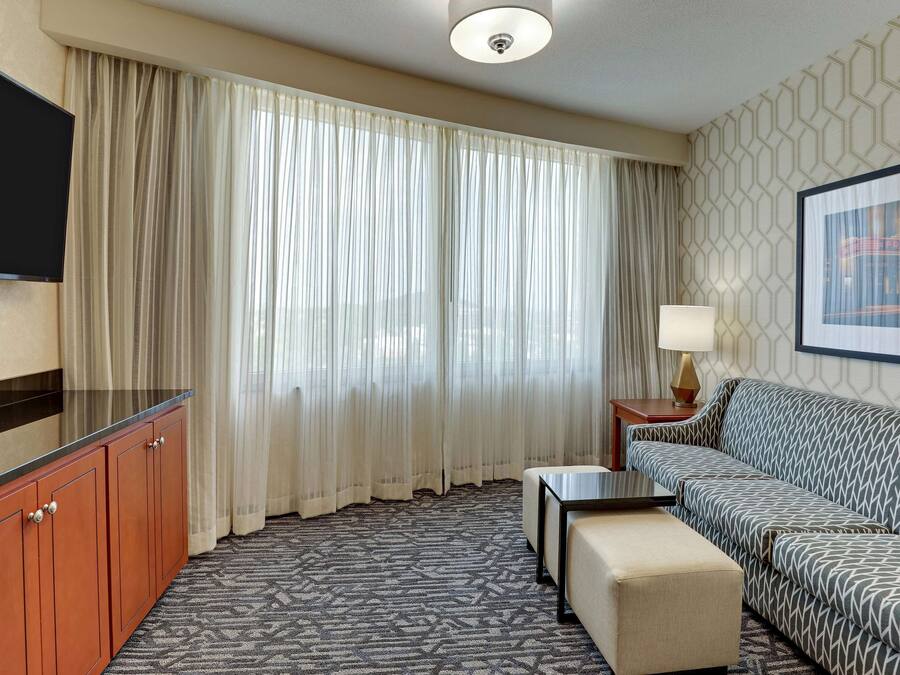 Une chambre d’hôtel avec un canapé, une télévision, un bureau et une fenêtre avec des rideaux.