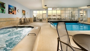An indoor swimming pool with a hot tub, lounge chairs, and a view of the city through large windows.