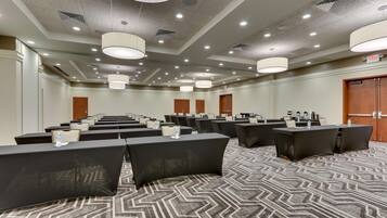 A conference room with multiple tables and chairs, ceiling lights, and a patterned carpet.