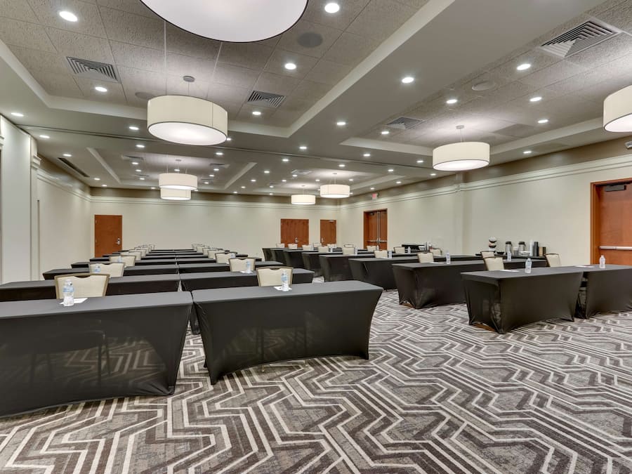 A conference room with multiple tables and chairs, ceiling lights, and a patterned carpet.