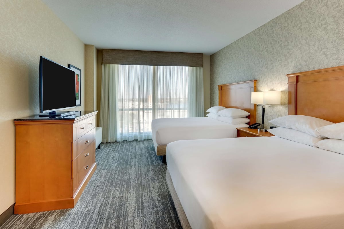 A hotel room with two beds, a TV, a desk, and a lamp.