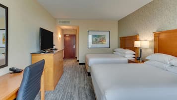 A hotel room with a bed, a desk with a chair, a television, a dresser, and a framed picture on the wall.