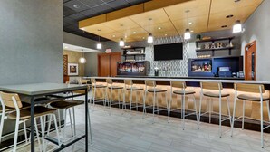 A modern bar area with a long counter, multiple bar stools, and a television screen above the bar.