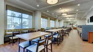 A spacious dining area with multiple tables and booths, large windows, and ceiling lights.