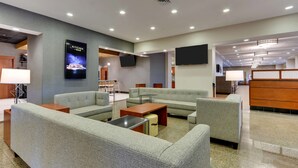 A modern hotel lobby with seating areas, a kitchen bar sign, and a reception desk.