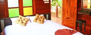 Una habitación de madera con una cama, dos almohadas, una colcha roja y un armario de madera.