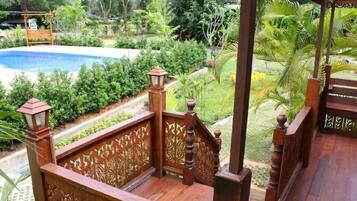Una terraza de madera con barandillas detalladas, con vistas a una piscina y abundante vegetación.