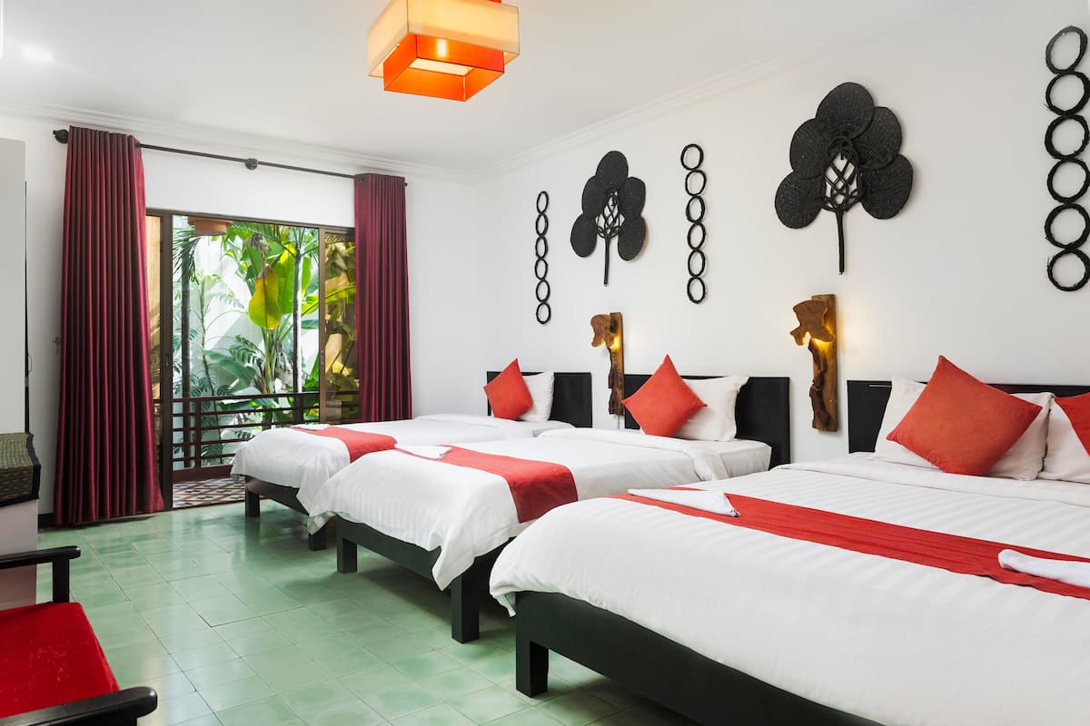 Ein Hotelzimmer mit zwei Betten, roter und weißer Bettwäsche, einem großen Fenster mit roten Vorhängen und Blick ins Grüne.