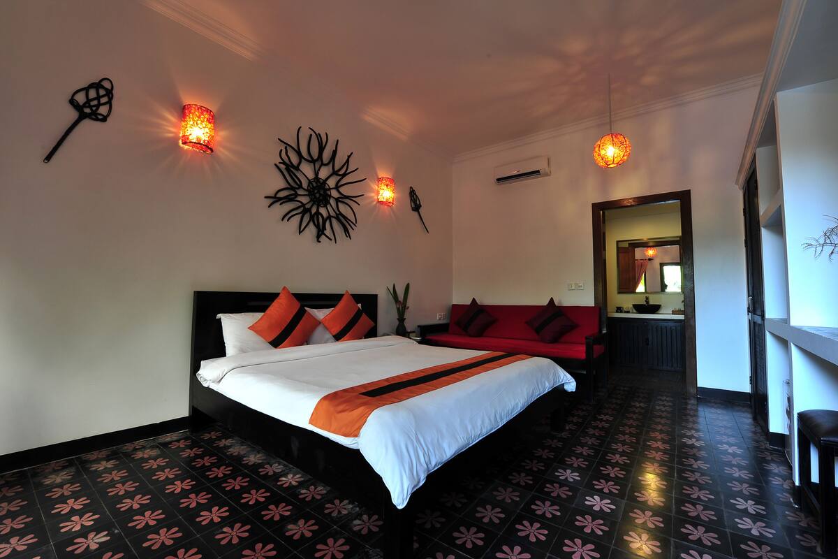 Ein Hotelzimmer mit einem Bett, einem roten Sofa, einem Wandbild und einem Flur, der zu einer Küche führt.