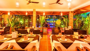A restaurant with tables set for dining, ceiling fans, and a view of a water feature.