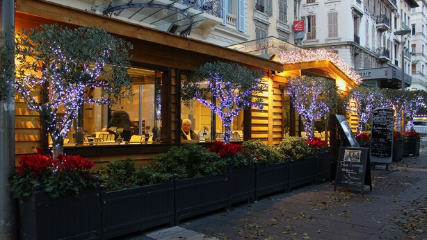 Un ristorante con posti a sedere all'aperto, decorato con luci viola e fiori rossi.