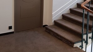 Una zona con tappeto che conduce a una porta con il numero 321, una scala con ringhiera in legno e una parete bianca.