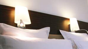 Una camera d'albergo con due letti, ognuno con lenzuola bianche e due lampade sui comodini.