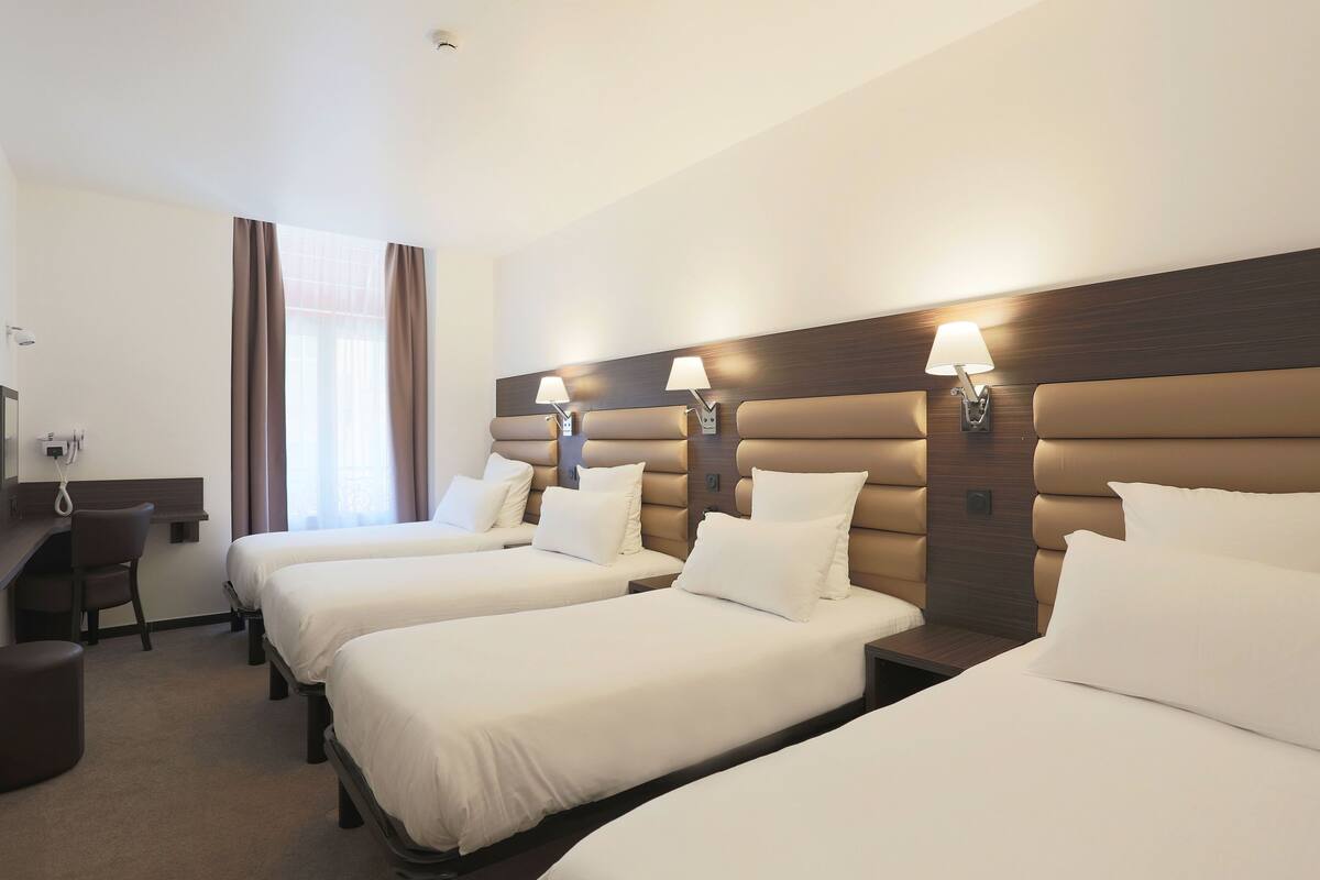 A hotel room with three single beds, a desk, and a chair.