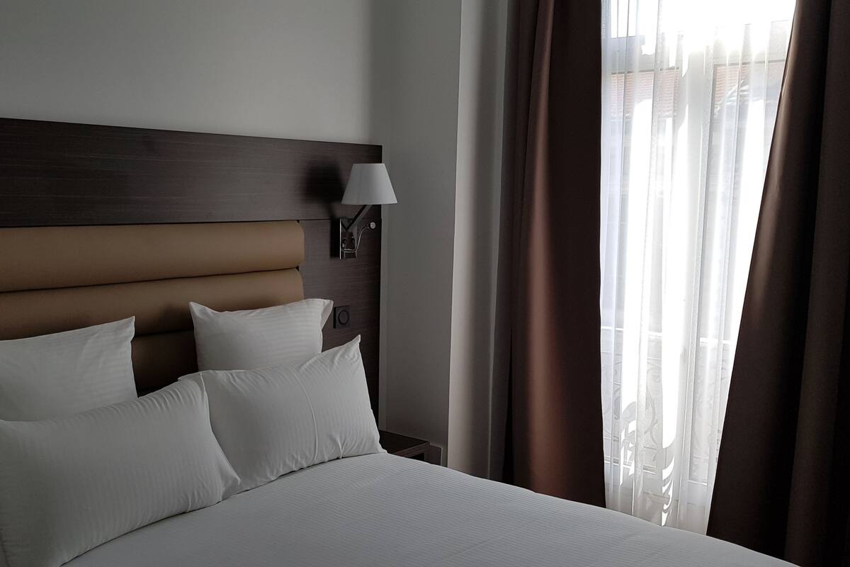 A hotel room with a large bed, two bedside lamps, and a window with curtains.